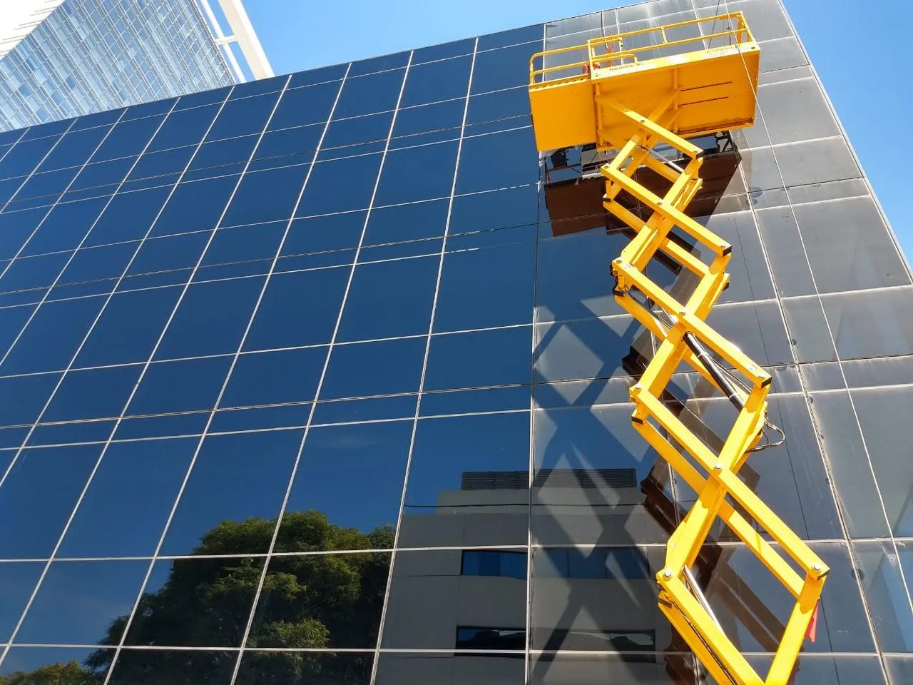 Plataforma elevadora amarilla junto a una fachada vidriada.